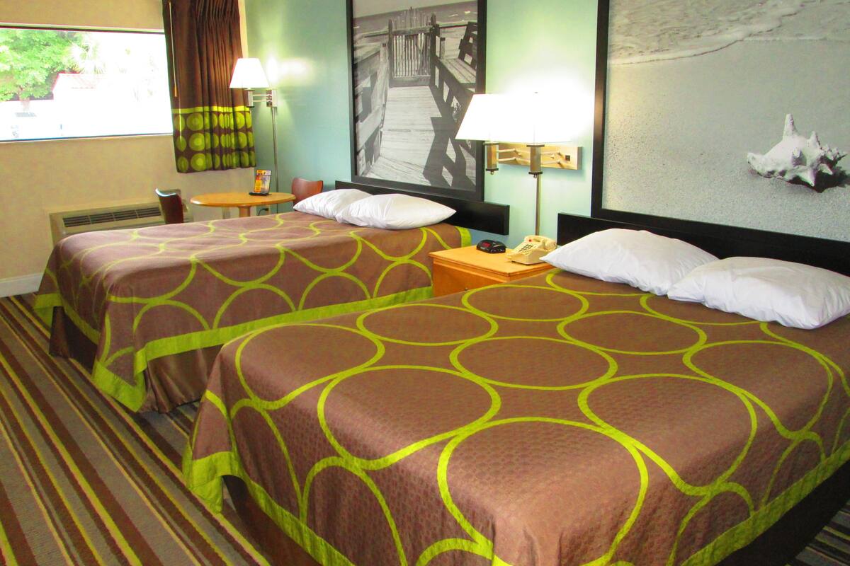 Une chambre d’hôtel avec deux lits, un bureau, une chaise, une lampe et un tableau au mur.