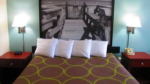 Een hotelkamer met een bed, twee nachtkastjes, een telefoon en een kunstwerk aan de muur waarop een pier afgebeeld is.