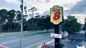 Een Super 8 bord met een bordje voor gratis Wi-Fi, gelegen op een straat hoek met bomen en een parkeerplaats op de achtergrond.