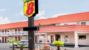 Een hotel met een dak van rode tegels, een opvallend 'Super 8' bord en een parkeerplaats met een witte auto.