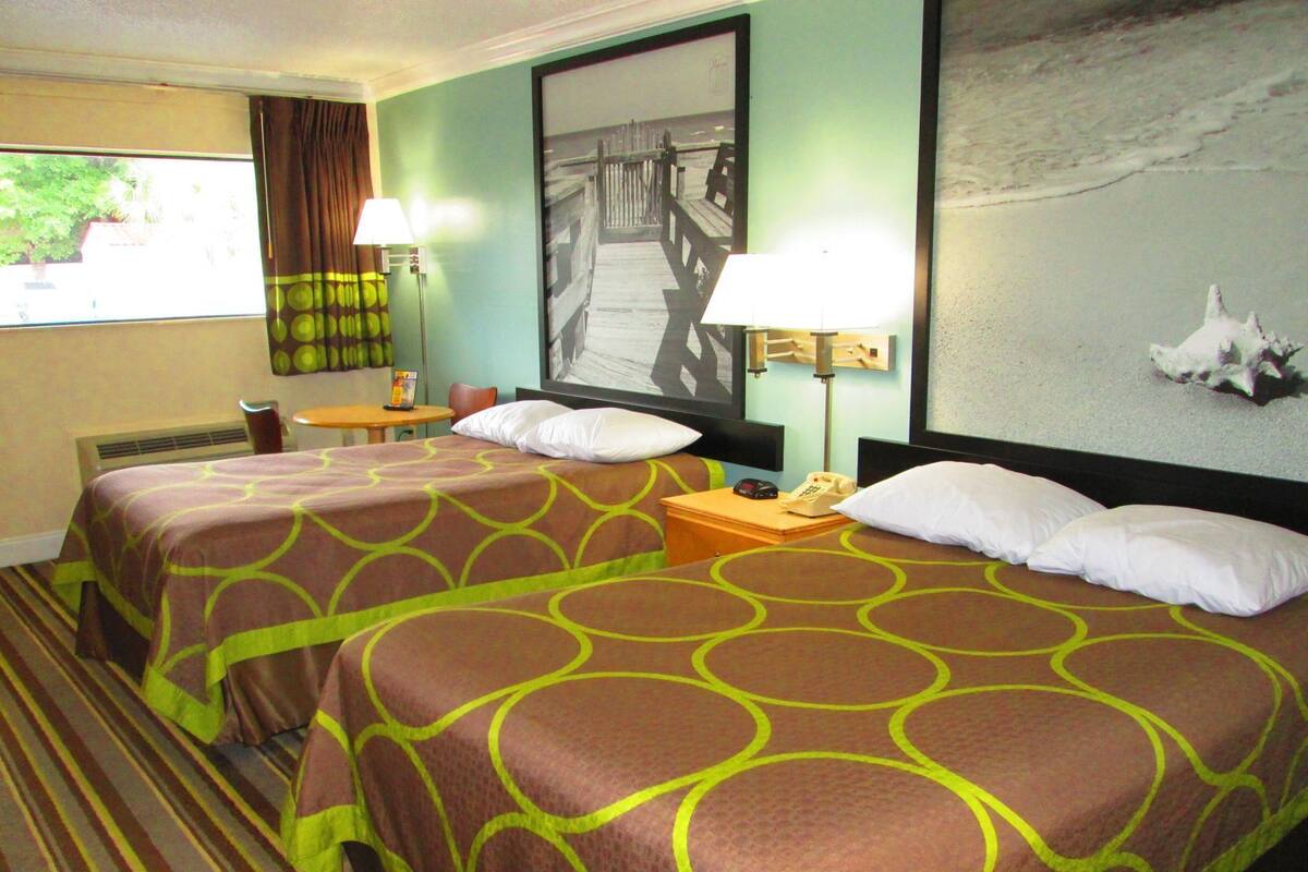 Une chambre d’hôtel avec deux lits, un bureau, une chaise, une lampe et un tableau au mur.