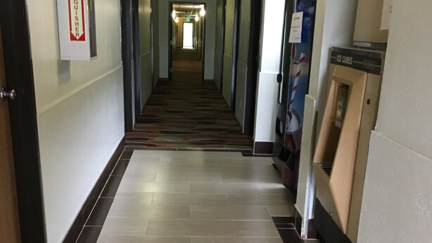 Un couloir d’hôtel avec un panneau indiquant l’emplacement d’un extincteur, un panneau de signalisation pour la sortie et un distributeur automatique.