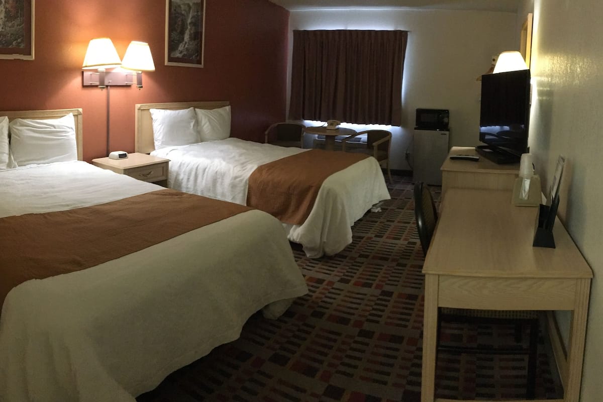 Une chambre d’hôtel avec deux lits, un bureau, une chaise, une télévision et une lampe.