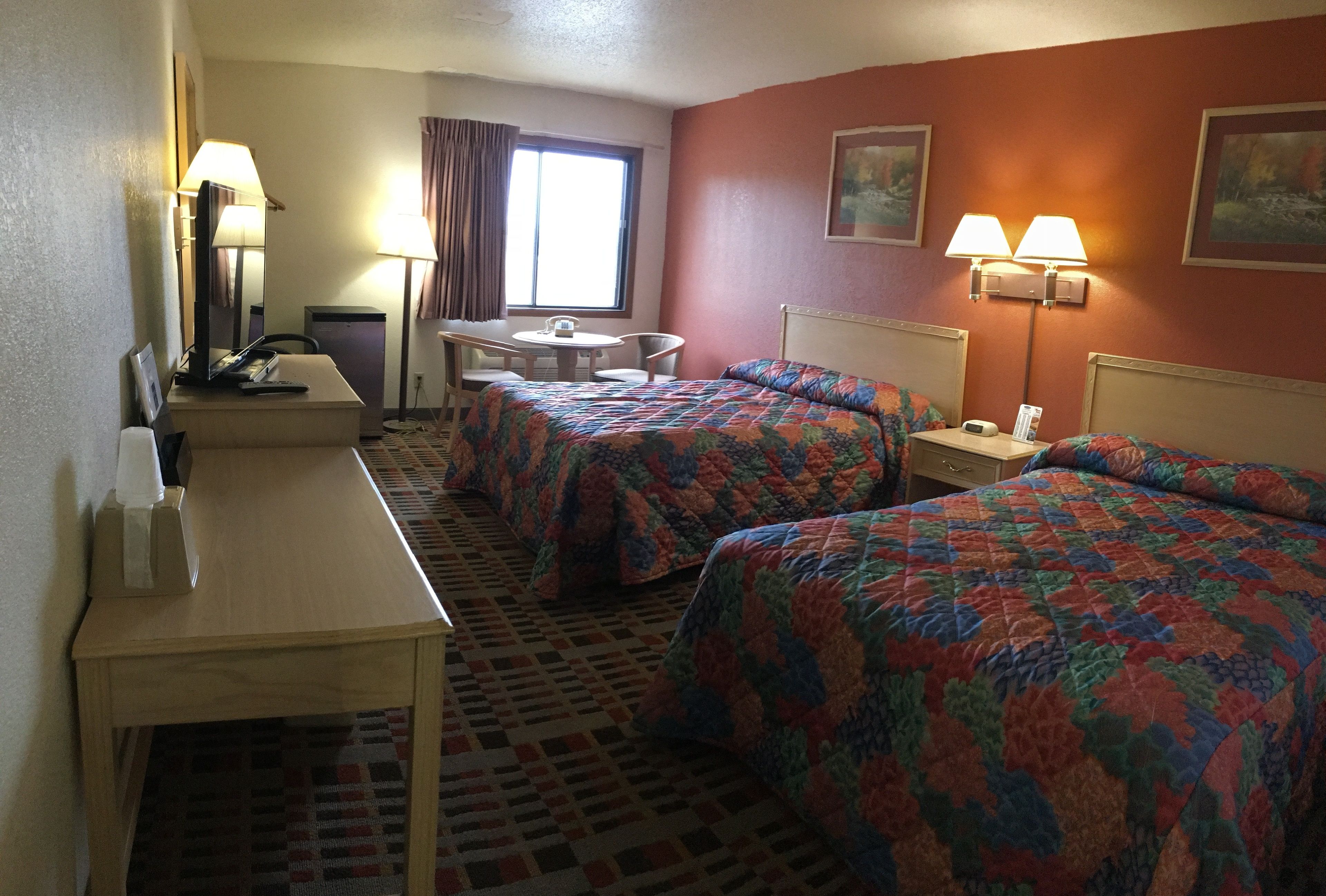 A hotel room with two beds, a desk, a chair, a small table, and a window with curtains.