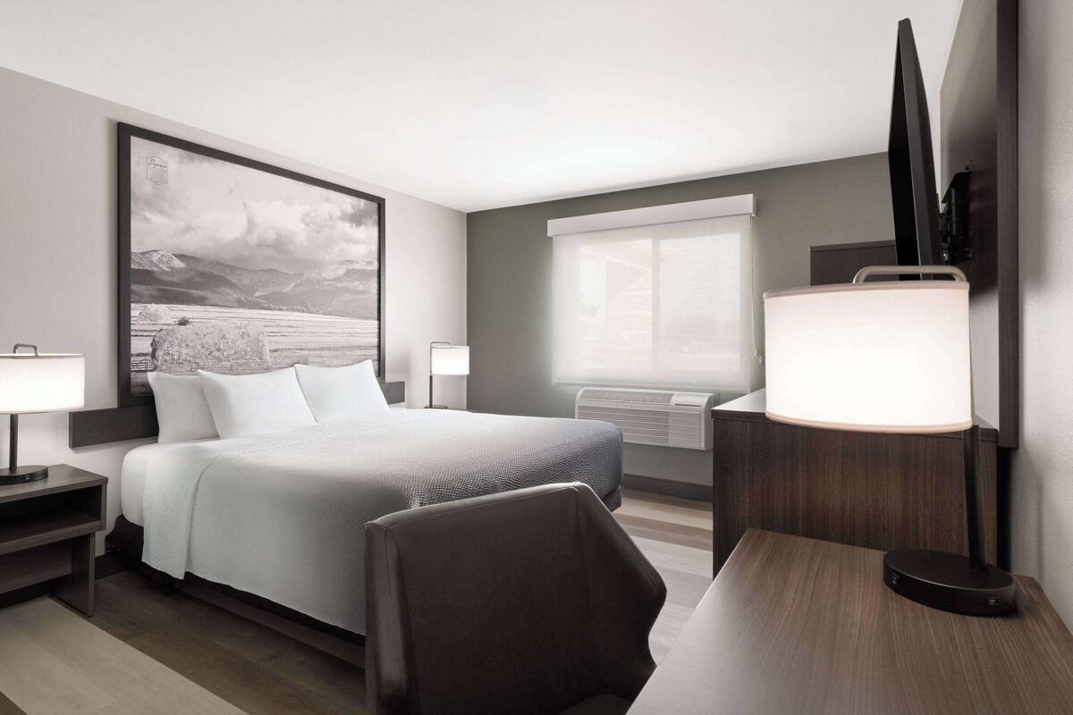 Habitación de hotel moderna con una cama grande, mesitas de noche, un escritorio, una silla, un televisor de pantalla plana y un ventanal amplio.