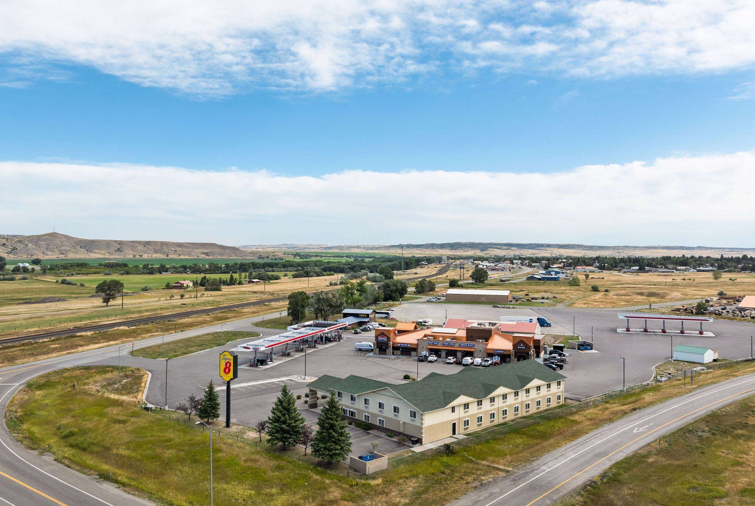 Une station-service avec un grand bâtiment au premier plan, une autoroute et des champs ouverts en arrière-plan.