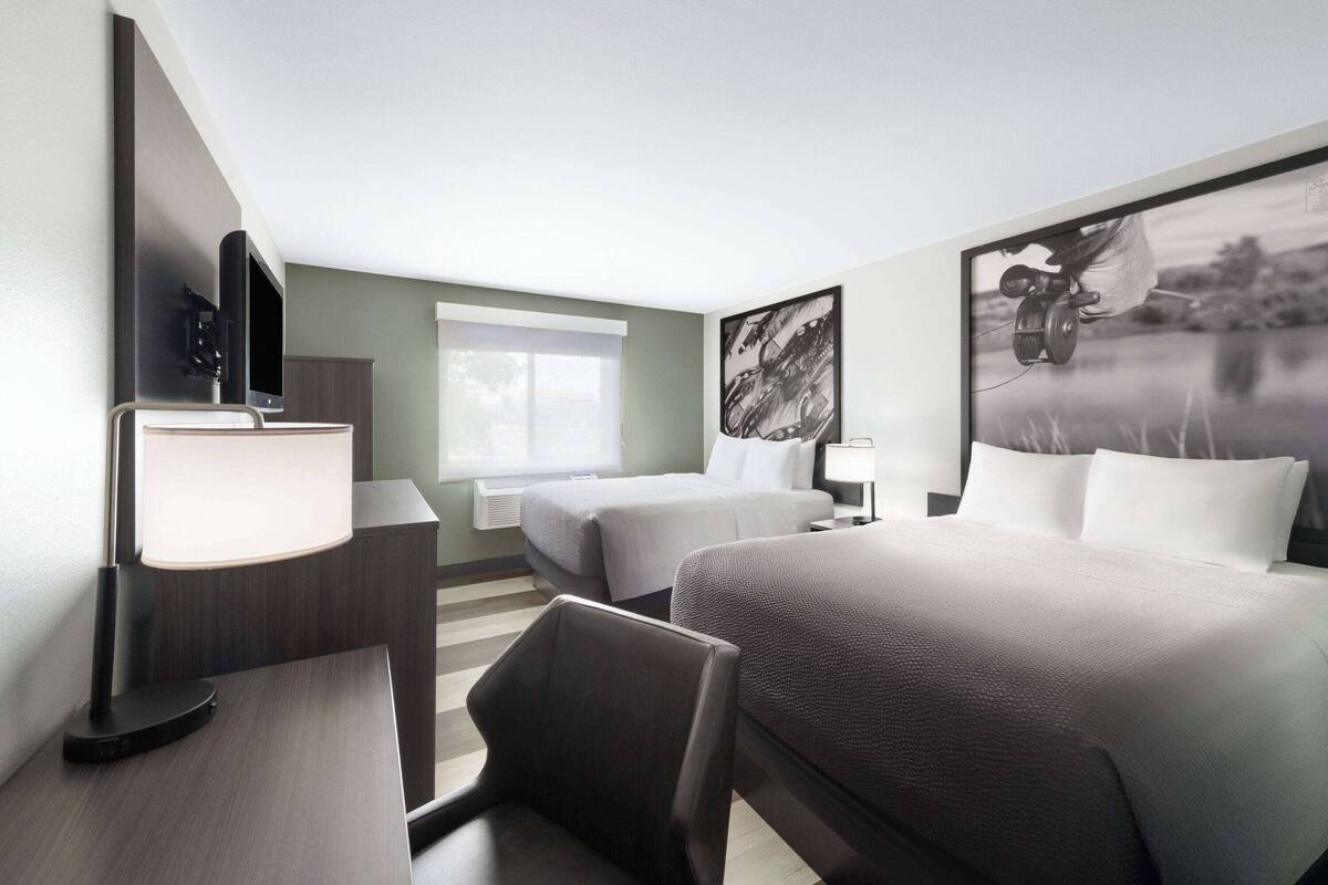 Habitación de hotel con dos camas, un escritorio con lámpara, televisor y un ventanal amplio.