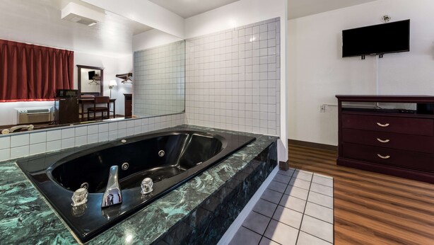 A modern bathroom with a large bathtub, a vanity with a mirror, and a flat-screen TV mounted on the wall. - Super Stay Plus (Morristown)