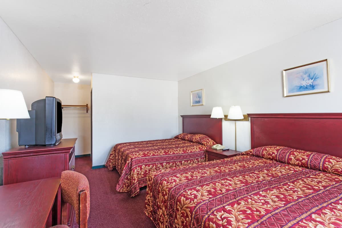 A hotel room with two beds, a TV, a desk, and a chair.