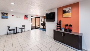 A hotel lobby with a reception desk, a television mounted on the wall, and a seating area with two chairs and a table. - Super Stay Plus (Morristown)