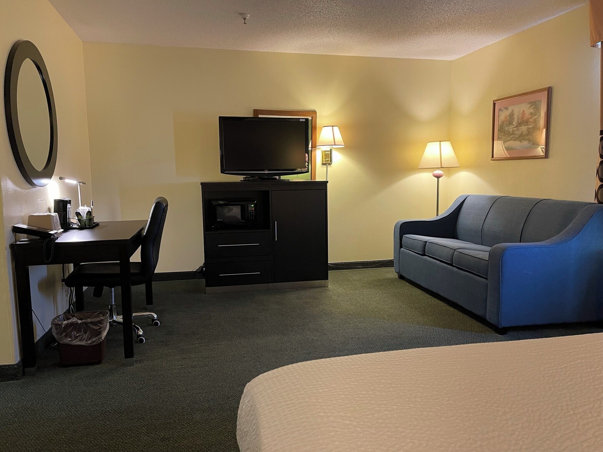 A hotel room with a bed, a desk with a computer, a television, a blue sofa, and a lamp.