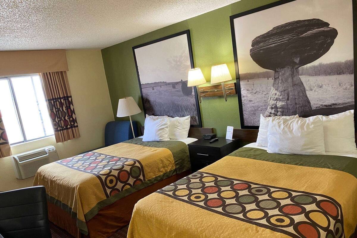 Habitación de hotel con dos camas, una ventana con cortinas, una lámpara de pared y un cuadro grande con un árbol.