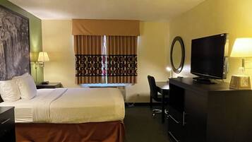 A hotel room with a bed, desk, chair, television, and a painting on the wall.