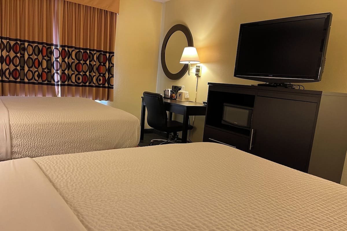 Habitación de hotel con dos camas, un escritorio con silla, una televisión y una lámpara.