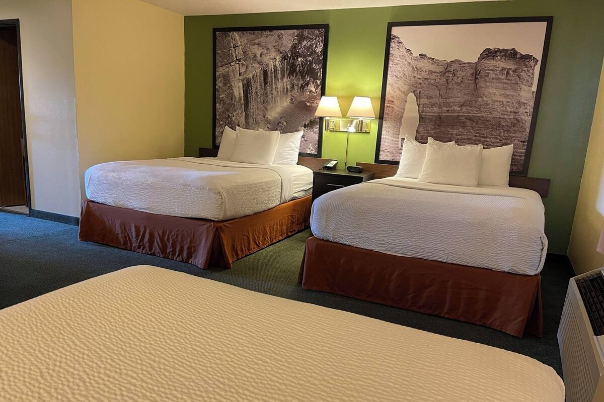 Habitación de hotel con dos camas individuales, una cama grande, una mesita de noche con lámpara y dos lámparas de pared.