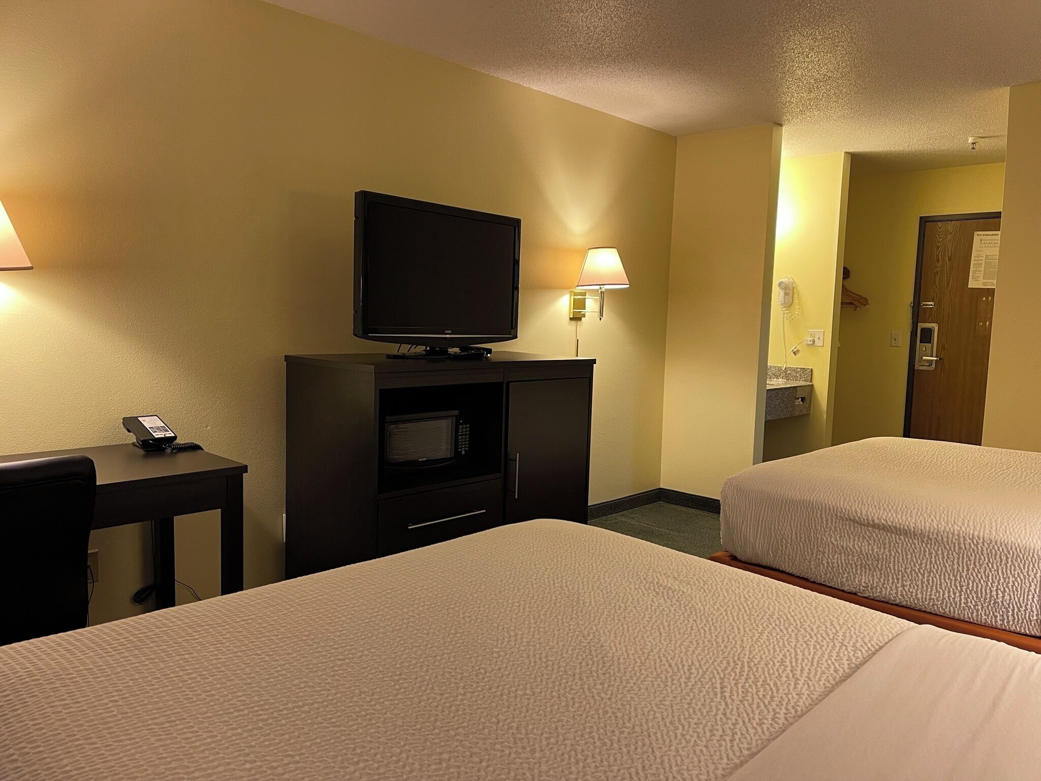 A hotel room with two beds, a television on a stand, a desk with a phone, and a lamp.
