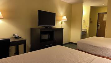 A hotel room with two beds, a television on a stand, a desk with a phone, and a lamp.