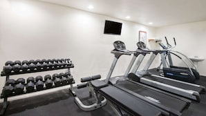 Un gimnasio equipado con cintas de correr, mancuernas y un televisor en la pared.
