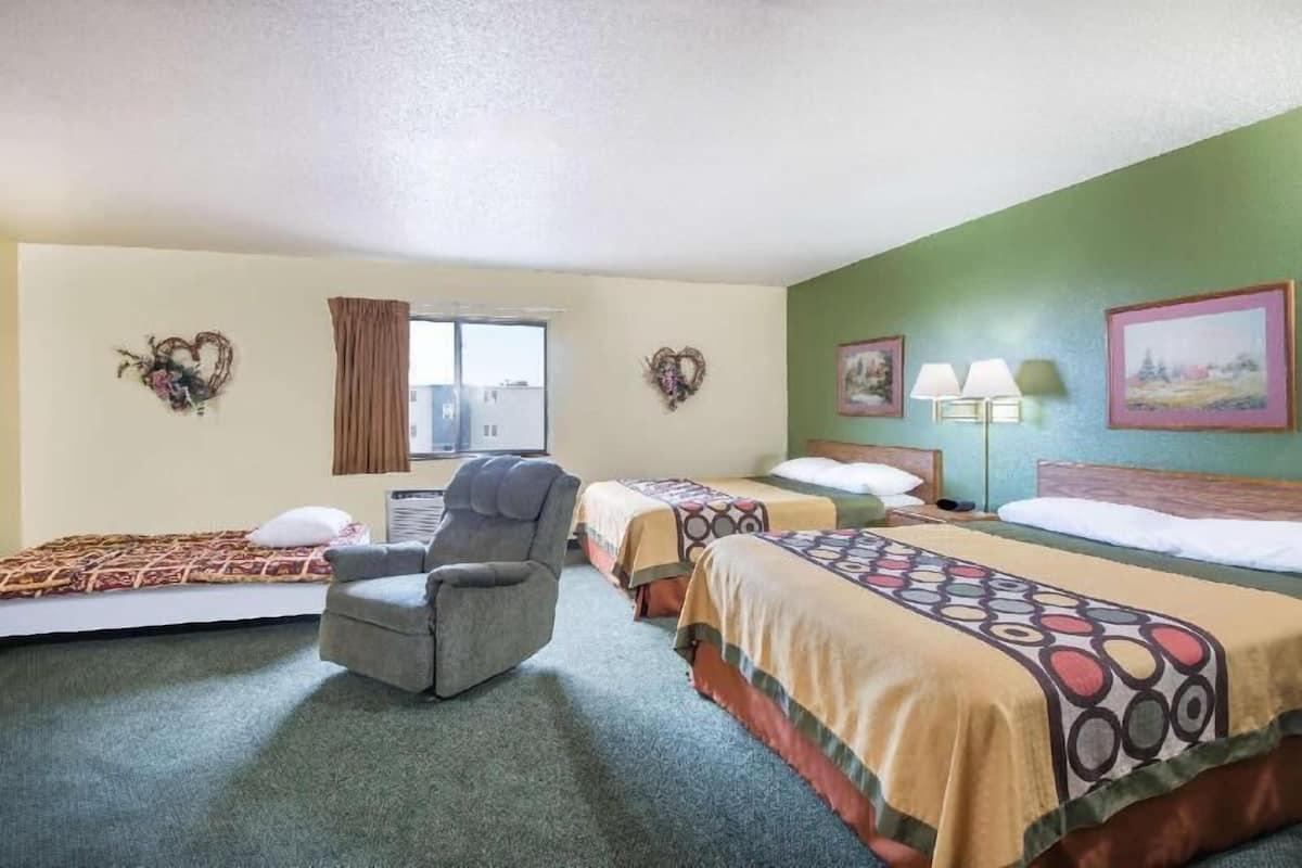 Habitación de hotel con dos camas, una silla, una ventana con cortinas y adornos en la pared.