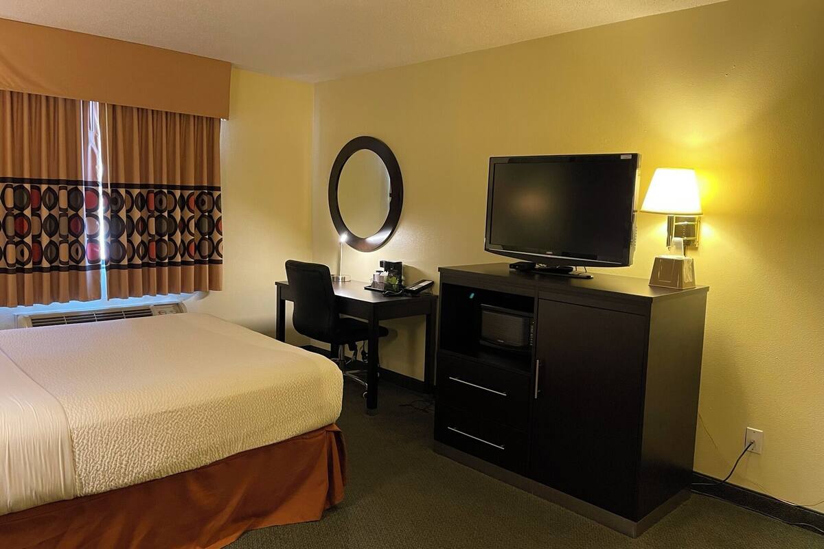 Una habitación de hotel con cama, escritorio, silla, televisor y lámpara.