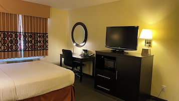 Una habitación de hotel con cama, escritorio, silla, televisor y lámpara.