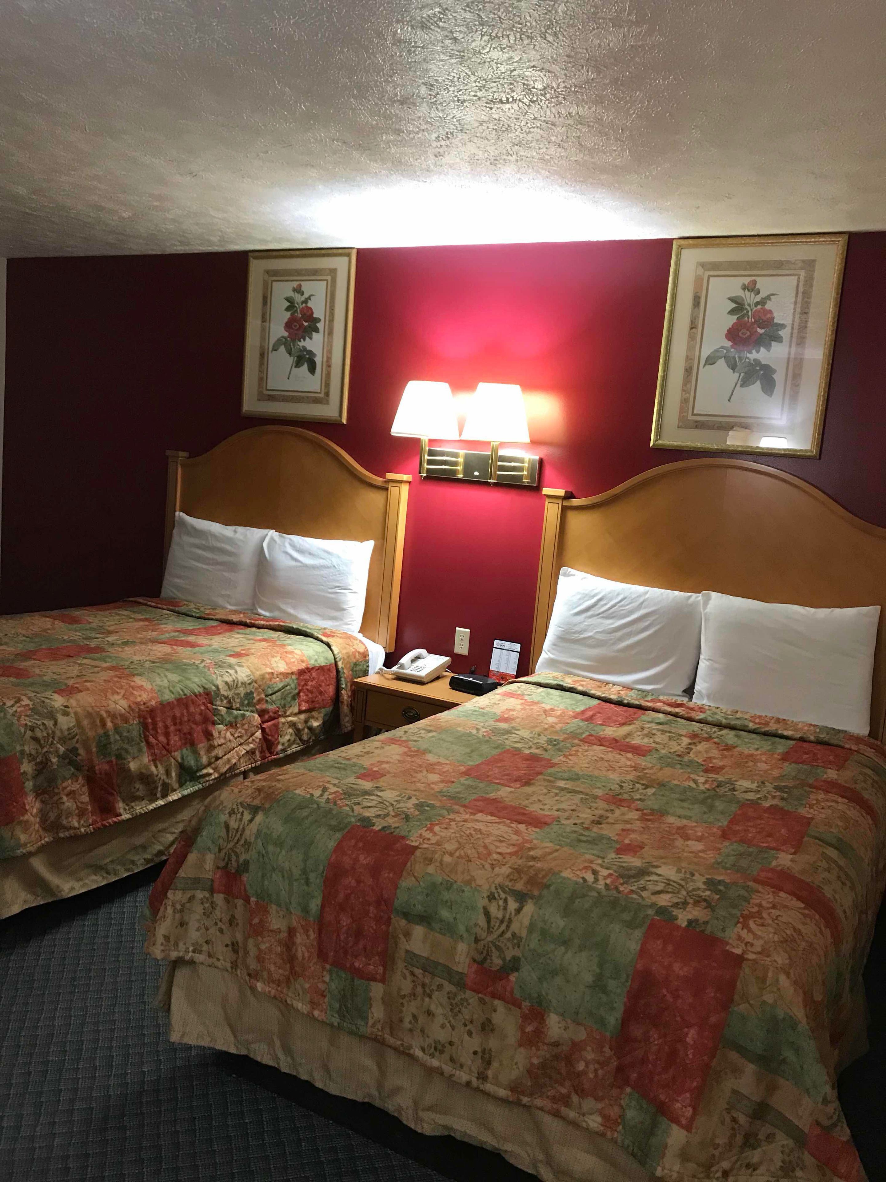 Habitación de hotel con dos camas, cada una con colcha floral, una mesita de noche con teléfono y una lámpara de pared.