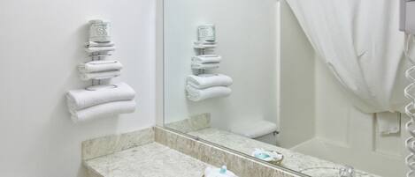 Un baño con lavamanos de mármol, un espejo grande, inodoro y cortina de ducha.