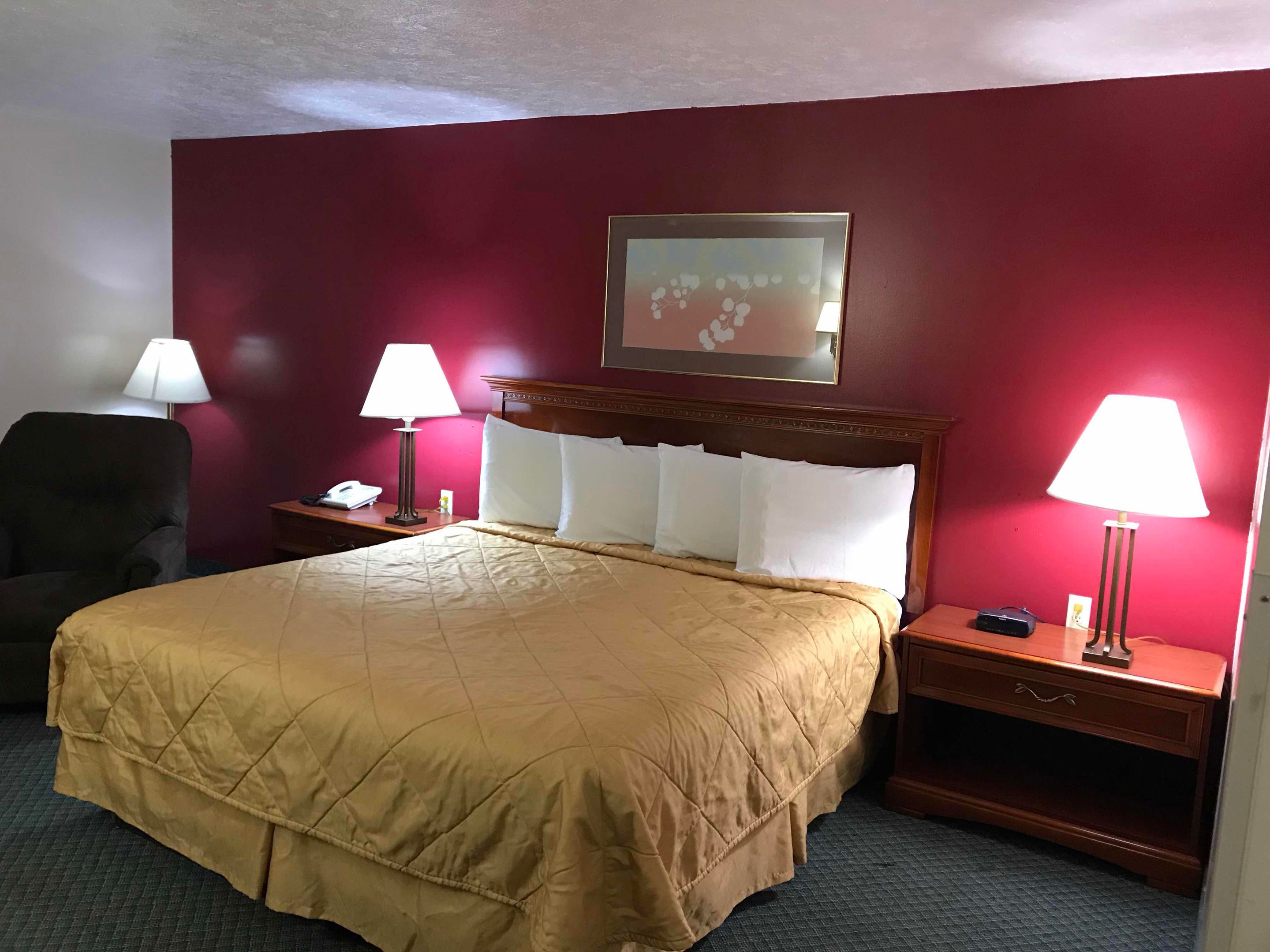 A hotel room with a large bed, two bedside lamps, a wooden nightstand, a chair, and a framed picture on the wall.