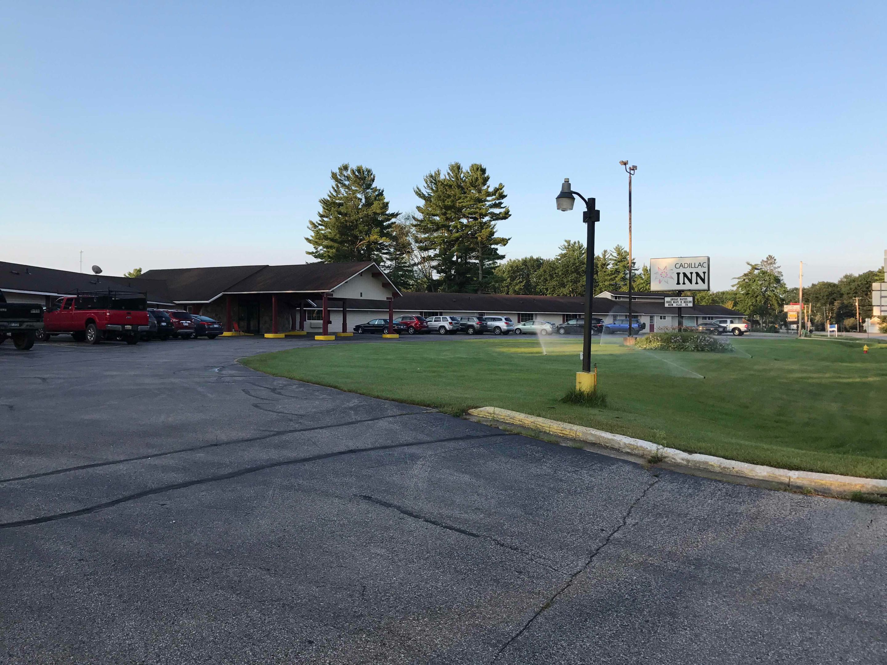 A parking lot with several cars, a red truck, and a building with a Cadillac Inn sign.