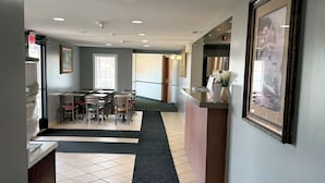 Un hall d’hôtel comprenant un comptoir d’accueil, un espace d’attente avec des chaises et des tables, une grande fenêtre et un tableau encadré au mur.