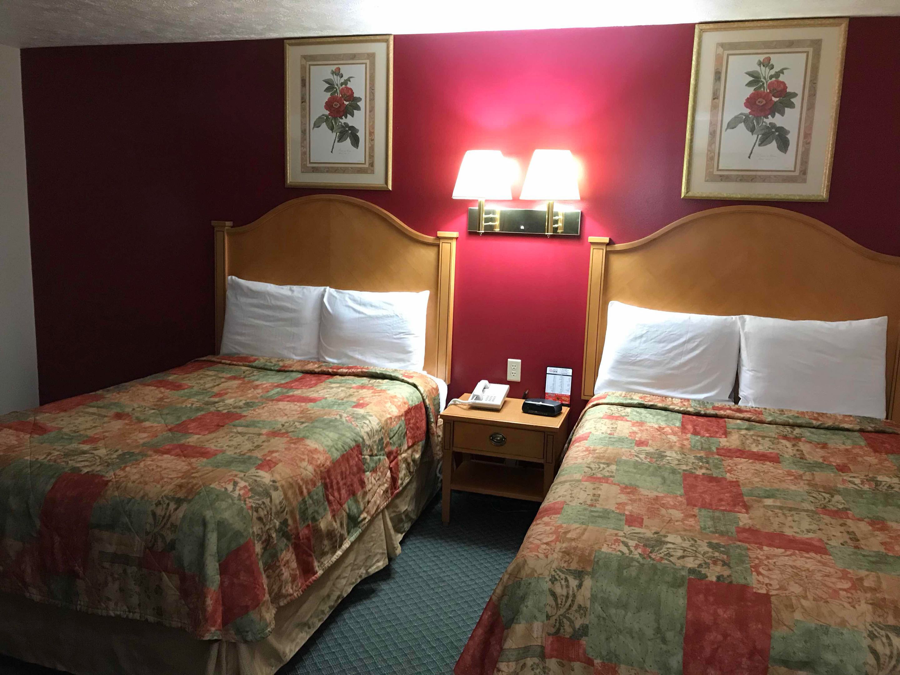 A hotel room with two beds, each with a floral bedspread, a nightstand with a phone and a lamp, and two framed floral pictures on the wall.