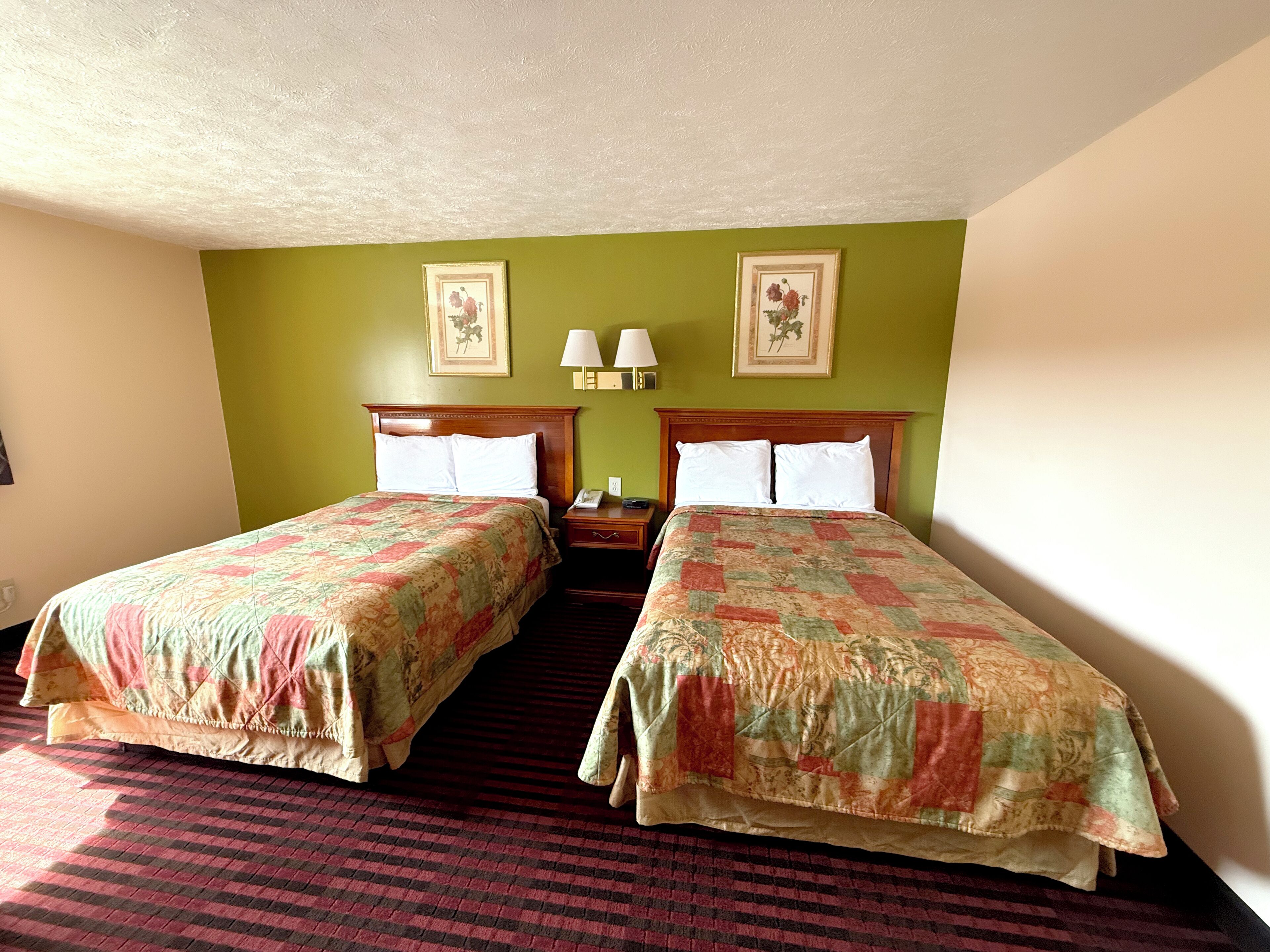 Habitación de hotel con dos camas, paredes verdes y alfombra roja.