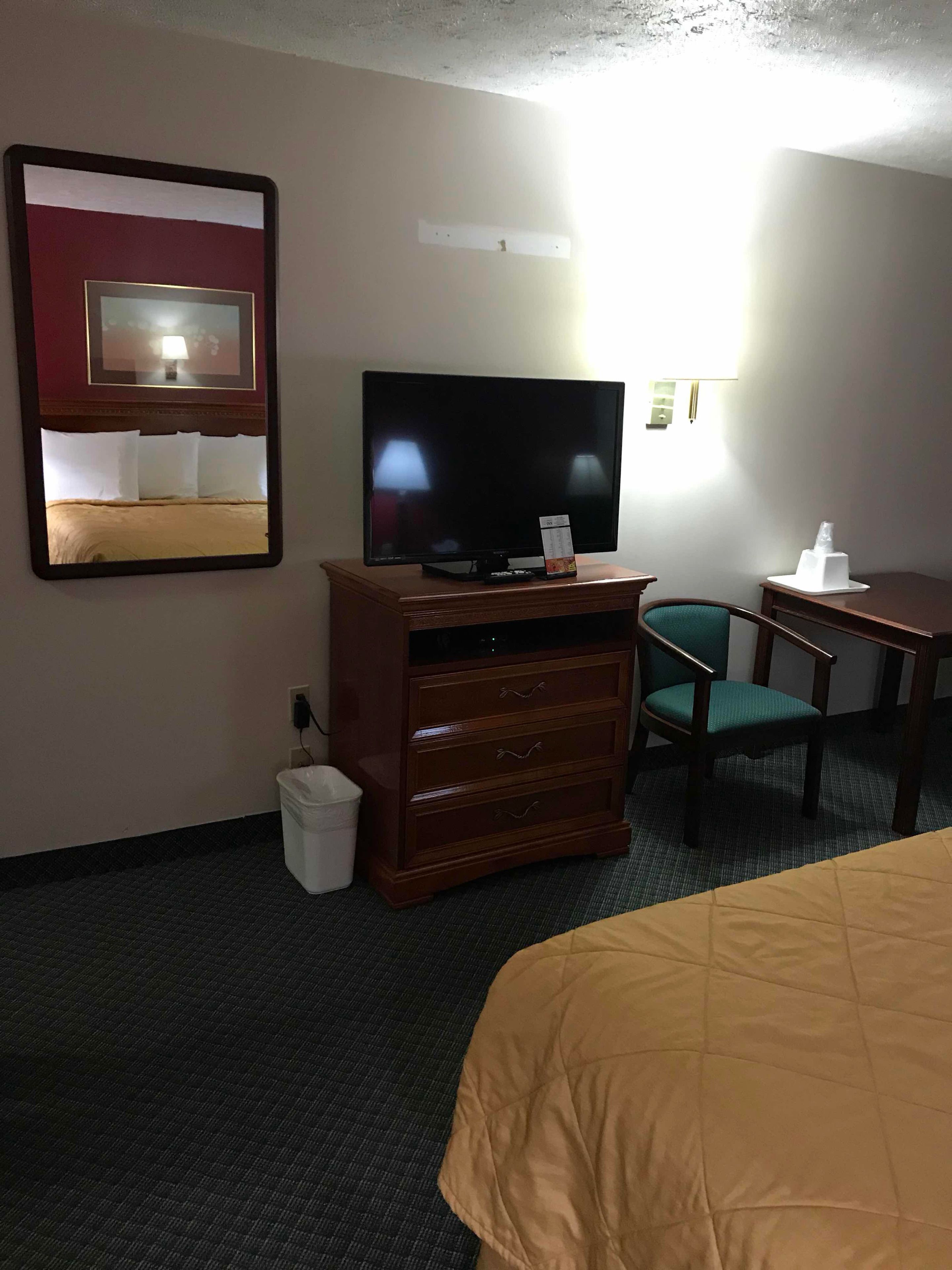 Una habitación de hotel con una cama, un aparador de madera con un televisor, una silla y una mesita.