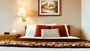 A neatly made bed with a patterned bedspread, a bedside lamp, a framed picture on the wall, and a wooden nightstand with a tissue box.