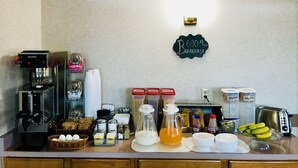 A breakfast setup with coffee machines, condiments, and a sign indicating breakfast hours.