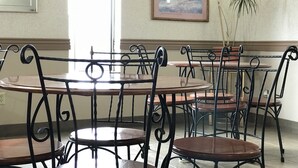 A dining area with round tables and chairs, a framed picture on the wall, and a potted plant.