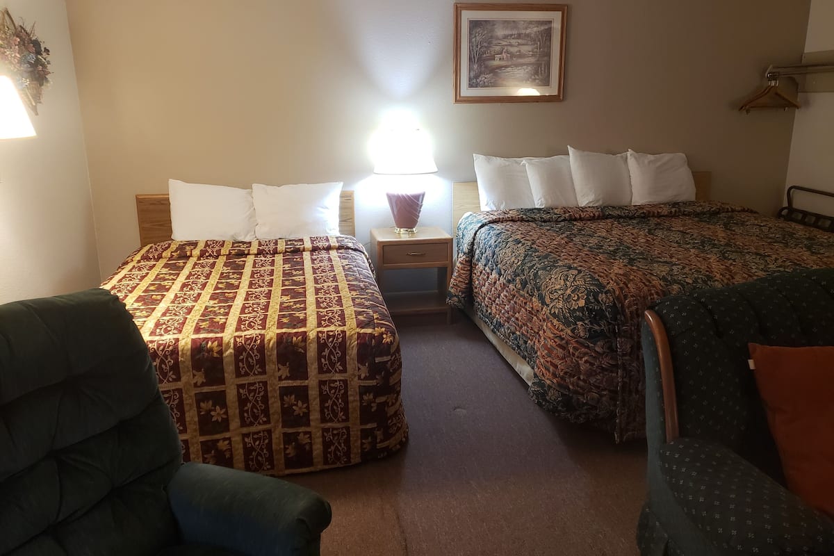 A hotel room with two beds, a nightstand, a lamp, a framed picture on the wall, and a chair.