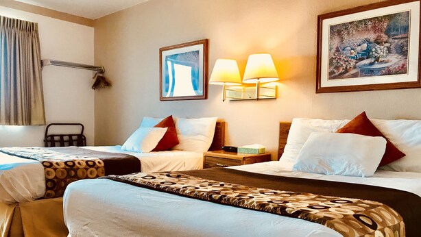 A hotel room with two beds, a bedside table, a chair, and a painting on the wall.