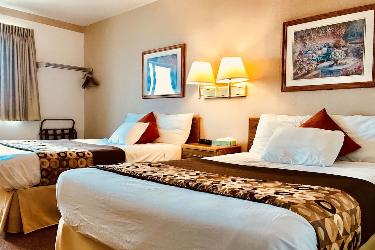 A hotel room with two beds, a bedside table, a chair, and a painting on the wall.