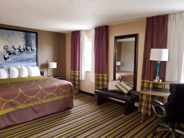 A hotel room with a large bed, a desk, a chair, a mirror, and a painting of horses on the wall. - Super 8 by Wyndham Bozeman (Bozeman)