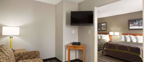 A hotel room with a sofa, a TV mounted on the wall, a small table, and a bed with a headboard.