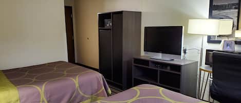 A hotel room with two beds, a TV, a desk, a chair, and a lamp.