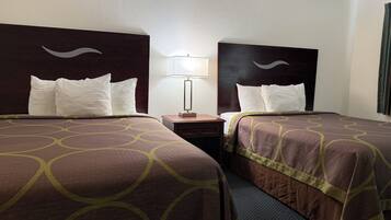 A hotel room with two beds, each with a headboard, a bedside table with a lamp, and a window with curtains.