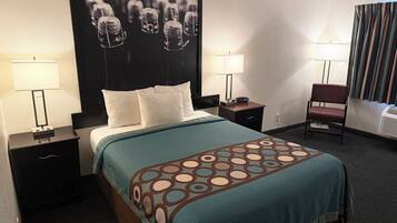 Habitación de hotel con cama, dos mesitas de noche, una silla, televisor montado en la pared y un cartel grande.