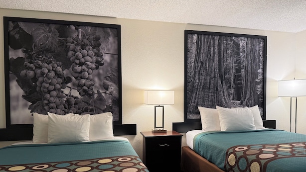 Une chambre d’hôtel avec deux lits, chacun recouvert d’une couvre-lit à motifs, une table de chevet avec une lampe et deux grandes images encadrées accrochées au mur.