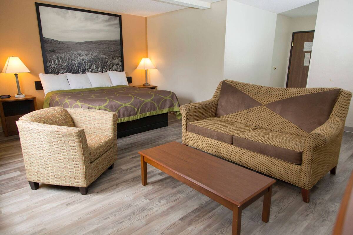 A hotel room with a bed, two chairs, a sofa, and a wooden table.