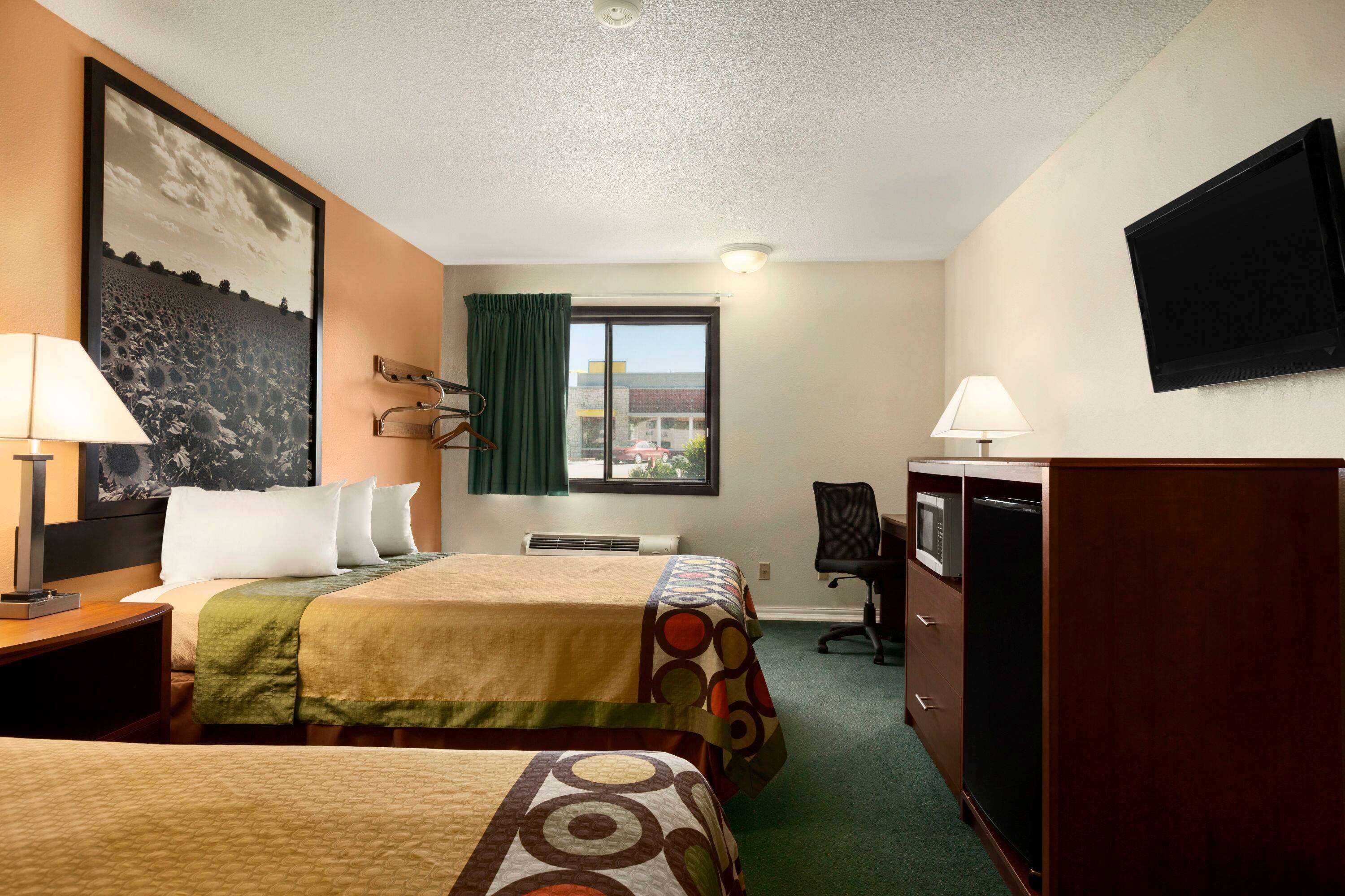 Habitación de hotel con dos camas, un escritorio con lámpara, televisor montado en la pared y ventana con vistas al exterior.