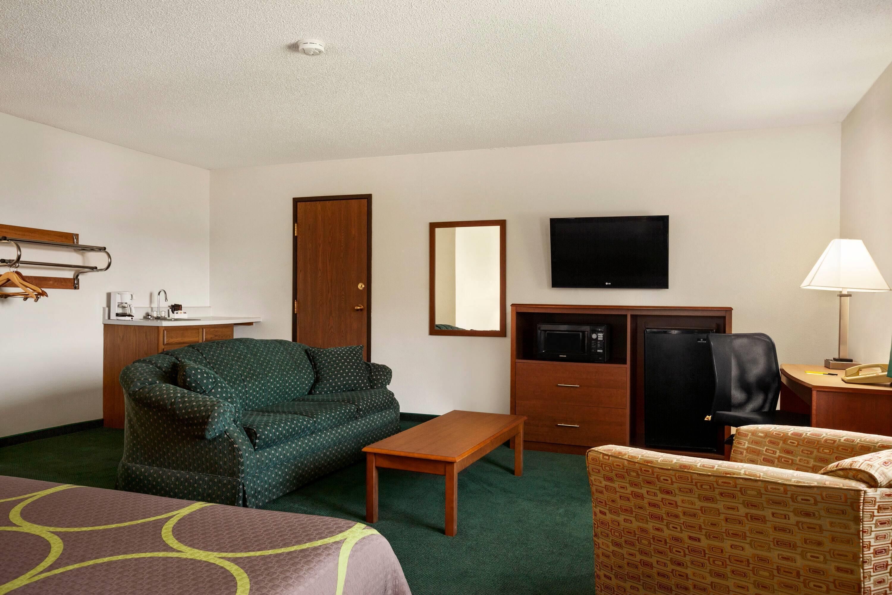 A hotel room with a bed, a sofa, a desk, a television, and a microwave.