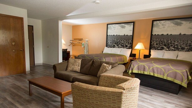 A hotel room with a bed, a sofa, a chair, a table, and two wall-mounted lamps. - Super 8 by Wyndham Concordia (Concordia)