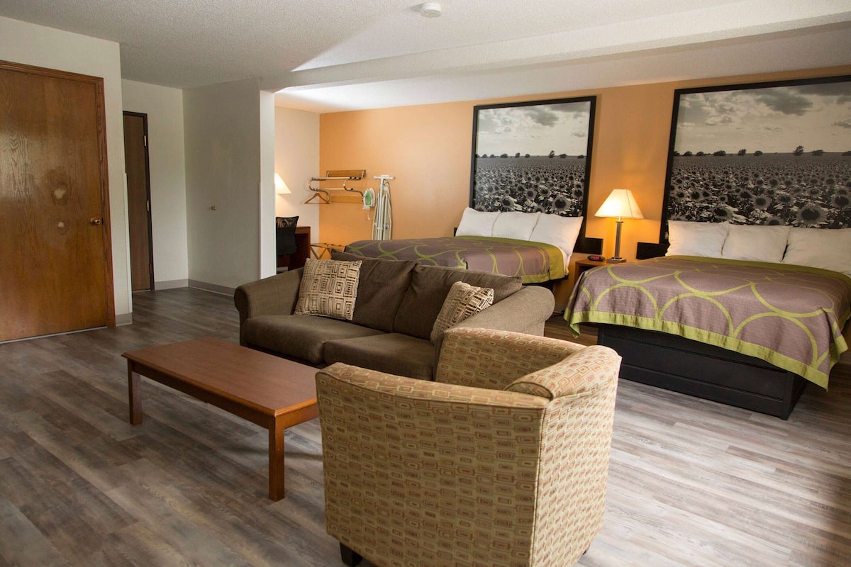 A hotel room with a bed, a sofa, a chair, a table, and two wall-mounted lamps.